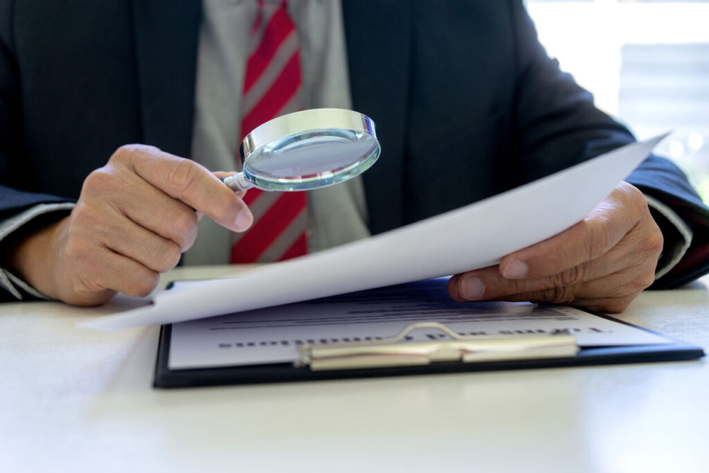 Person examining legal documents with a magnifying glass, symbolizing careful review during a federal investigation in California.